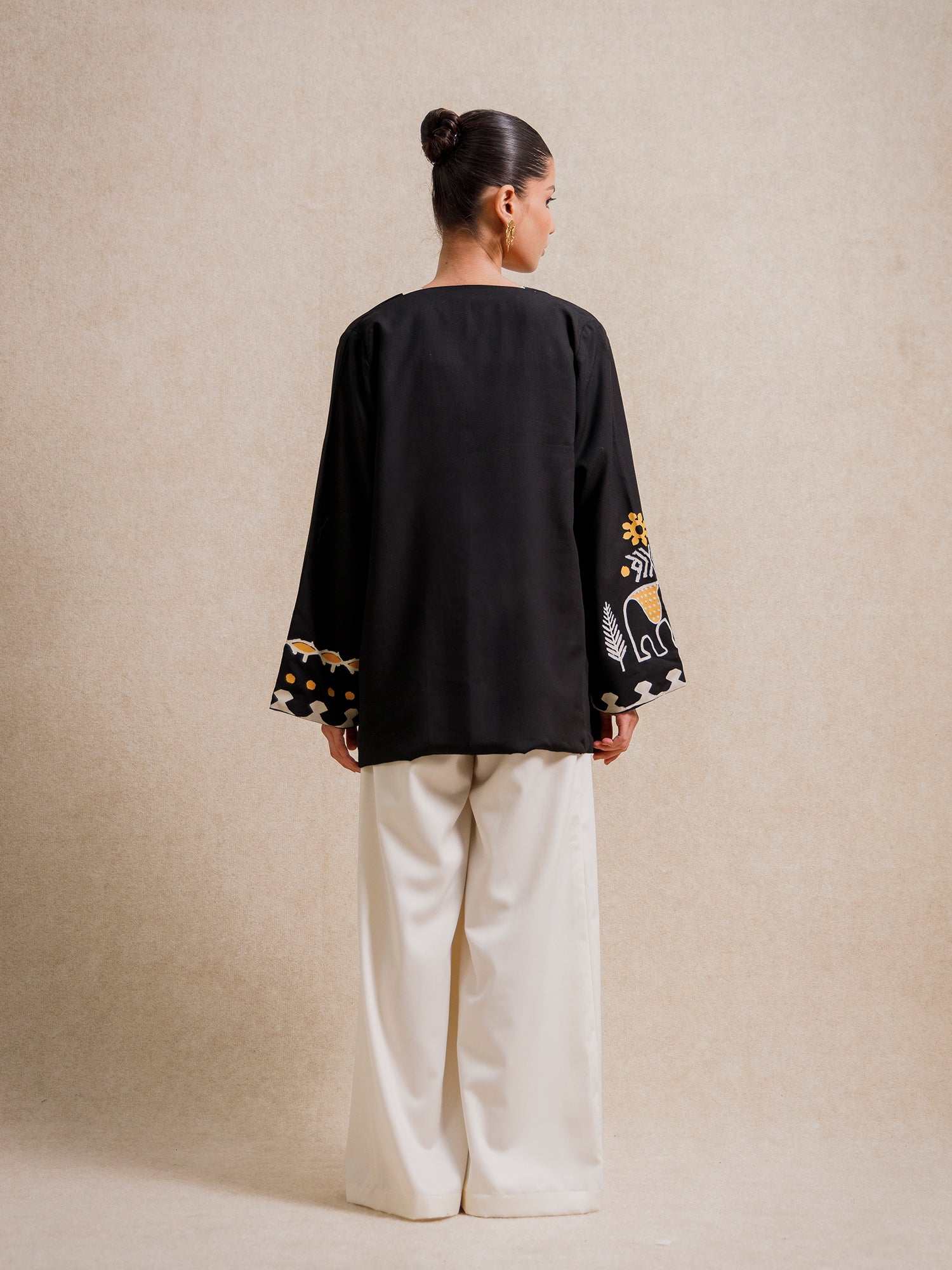 Back view of the Adara Black short kimono worn by a model, featuring hand-printed sleeve motifs on a beige background