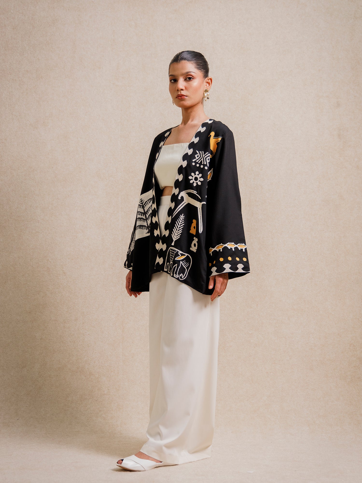 Side view of the Adara Black short kimono worn by a model, featuring hand-printed motifs on a beige background