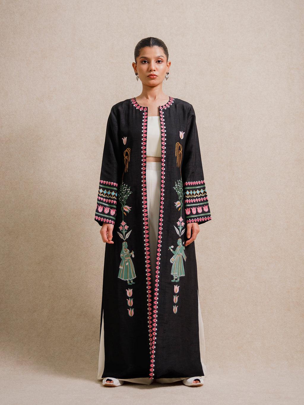 Model wearing the Courtyard Dance black long jacket with hand-printed figures and geometric borders against a neutral backdrop