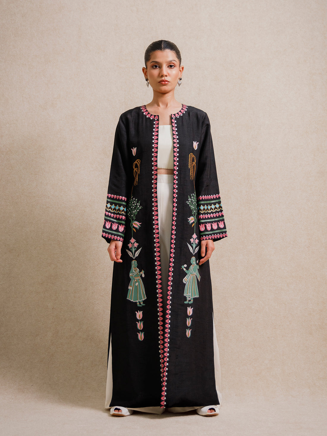 Model wearing the Courtyard Dance black long jacket with hand-printed figures and geometric borders against a neutral backdrop