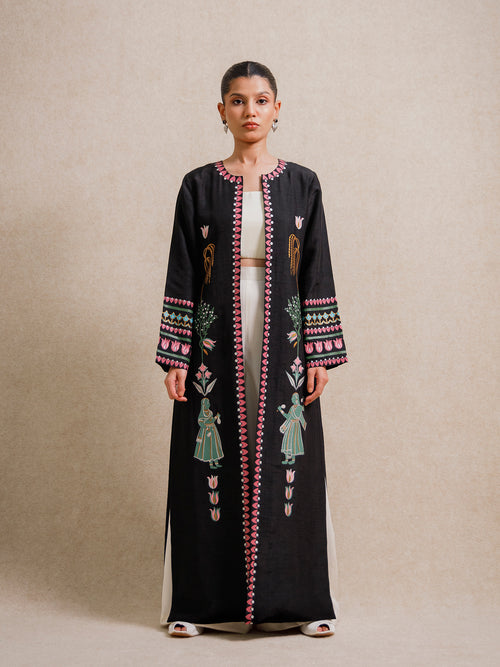 Model wearing the Courtyard Dance black long jacket with hand-printed figures and geometric borders against a neutral backdrop
