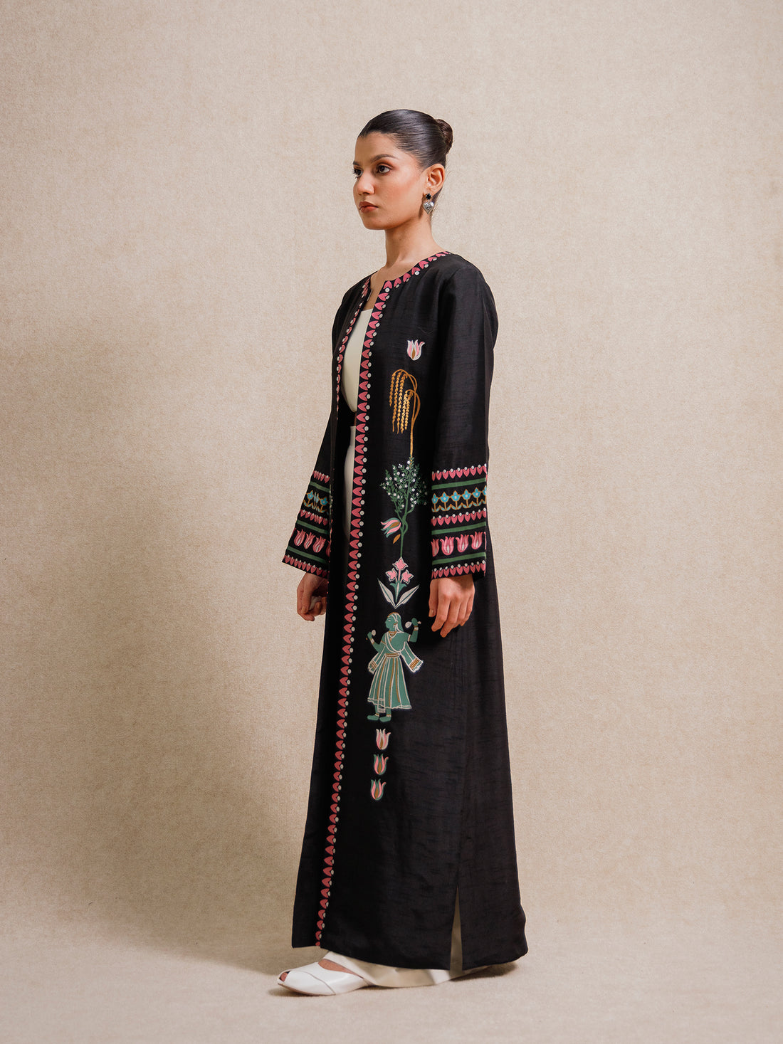 Model wearing the Courtyard Dance black long jacket with hand-printed figures and geometric borders against a neutral backdrop