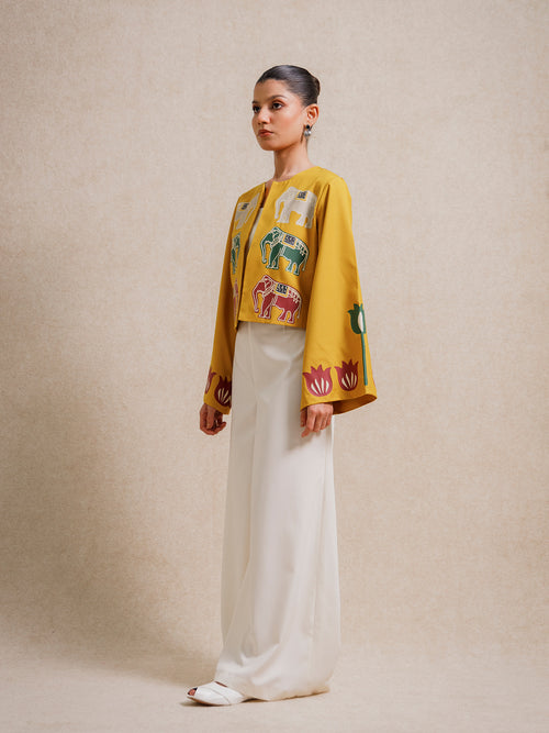 Side view of a model wearing the Alam Guman Ochre short jacket with hand-printed animal motifs, styled over a white outfit on a beige background